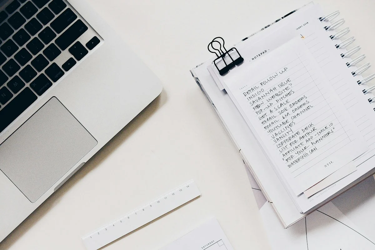 Laptop beside an open notebook with a to-do list, representing a shared knowledge base that documents how the team works