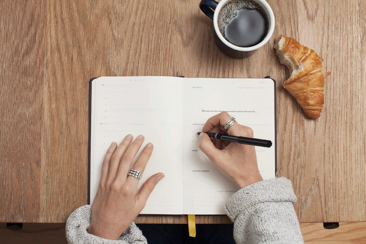 Person writing plans in a notebook at a desk, stepping back from client work to plan how the WordPress agency runs