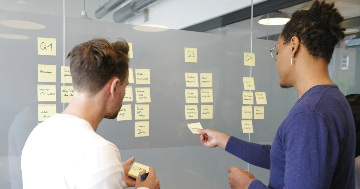 Two people planning a WordPress agency workflow with yellow sticky notes arranged in columns on a glass wall kanban board